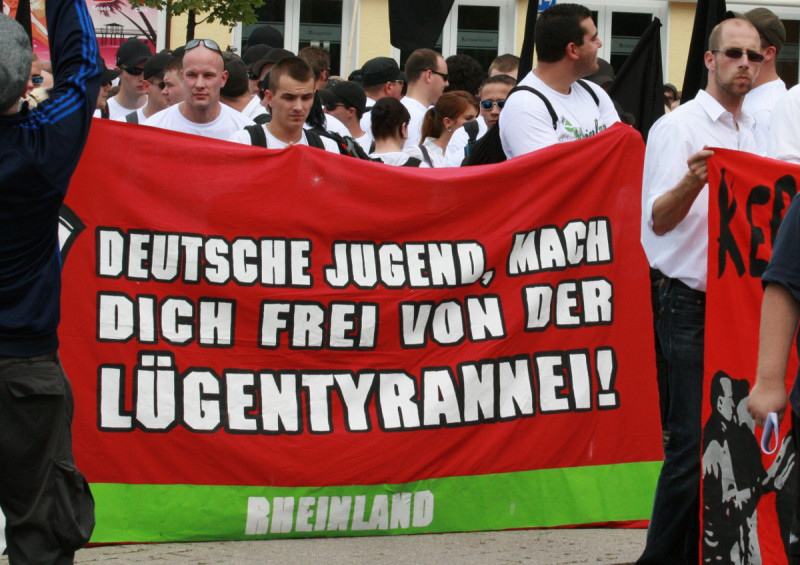 Das Transparent »Deutsche Jugend, mach die frei von der Lügentyrannei!« bezieht sich auf die im NS-Parole »Deutsche, macht euch frei von der Judentyrannei«.