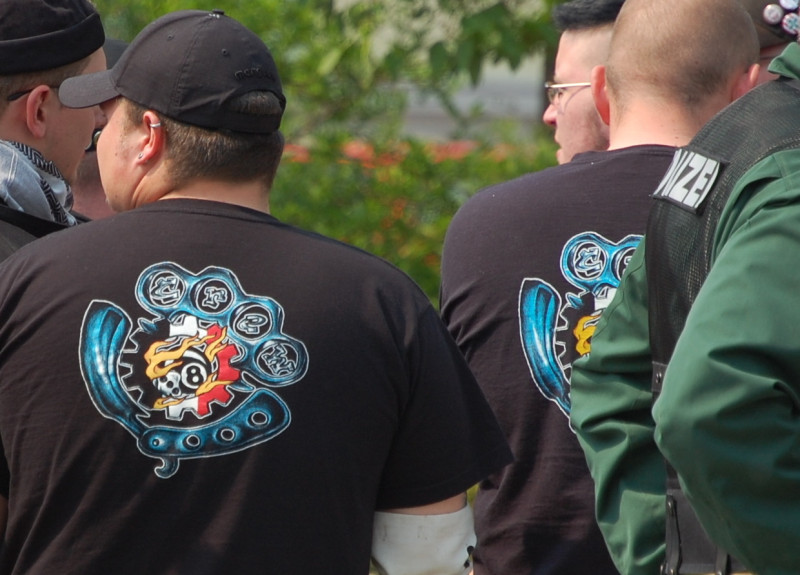 »Crew 38«-Erkennen für Fortgeschrittene. "Crew" steht in den Finger-Löchern des abgebildeten Schlagrings. Die »38« ist durch einen Würfel mit der 3 und eine Billardkugel mit der 8 (»Eightball«) dargestellt. Jedoch: Das schwarz-weiß-rote Zahnrad ist ein typisches Erkennungmerkmal von Hammerskins.