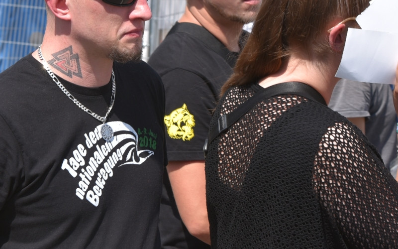 Das Bild zeigt die schwarz-weiß-rote Valknut als Halstätowierung und den brüllenden Bären, das Logo der neonazistischen Bekleidungsmarke Black Legion.