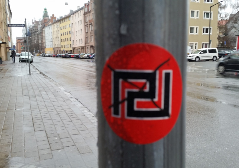 Foto aus Nürnberg 2016. Durch die farbliche Gestaltung des schwarzen Mäanders mit weißen Rand auf rotem Hintergrund werden die Assoziationen zum Hakenkreuz, bzw. zur Hakenkreuzfahne, verstärkt. 
Im Januar 2013 verbreitete sich die Nachricht über die Gründung eines offiziellen Ablegers der Chrysi Avgi in Nürnberg. Bei dieser »Nürnberger Zelle« handelte es sich um eine kleine Gruppe, die über eine Homepage ihre Gründung und die Durchführung einer Tagung bekannt gab und ein Gruppenfoto von sich verbreitete. Ihre Internetpräsenz war schon im Februar 2013 wieder offline. 
Darüber hinaus trat die Gruppe nicht in Erscheinung.
Nürnberg ist eine Schnittstelle zwischen deutschen und griechischen Neonazis. Die 2014 verbotene Neonaziorganisation Freies Netz Süd (FNS) hatte ihren Schwerpunkt in Nürnberg und unterhielt gute Kontakte zur Chrysi Avgi, die nach dem FNS-Verbot von der Partei Der Dritte Weg (eine Nachfolgeorganisation des FNS) weitergeführt wurden. Das Foto wurde in Nürnberg vor dem Wohnhaus eines Kader des FNS und des Dritten Wegs aufgenommen.