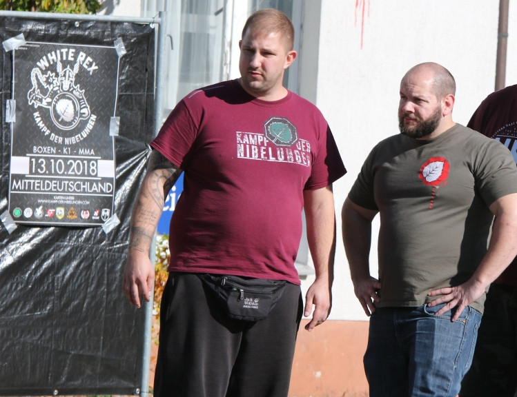 Foto vom Eingang einer Veranstaltung des Kampf der Nibelungen-Netzwerkes 2018 in Sachsen. Alexander Deptolla aus Dortmund (links) ist eine zentrale Figur im KdN, rechts ein NPD-Funktionär aus Hessen. Zu dieser Zeit kooperierte Kampf der Nibelungen eng mit dem neonazistischen Kampfsport-Label White Rex und führte mit diesem gemeinsame Veranstaltungen durch. Die (Geschäfts-)Beziehung zerbrach 2019, unter anderem im Streit um die Verteilung der Gelder.