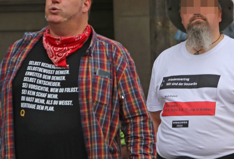 Anhänger der Reichsbürger und des QAnon-Verschwörungsmythos auf einer Reichsbürger-Kundgebung am 28. August 2020 in Berlin. Die Kernforderungen der Reichsbürger nach einem Friedensvertrag und nach Souveränität für Deutschland werden in dem Shirt-Motiv mit dem QAnon-Kürzel WWG1WGA verbunden. Auch die linke Person ist ein QAnon-Anhänger. Das Q steht für QAnon, "Vertraue dem Plan" (englisch: Trust the Plan) ist ein QAnon-Spruch.