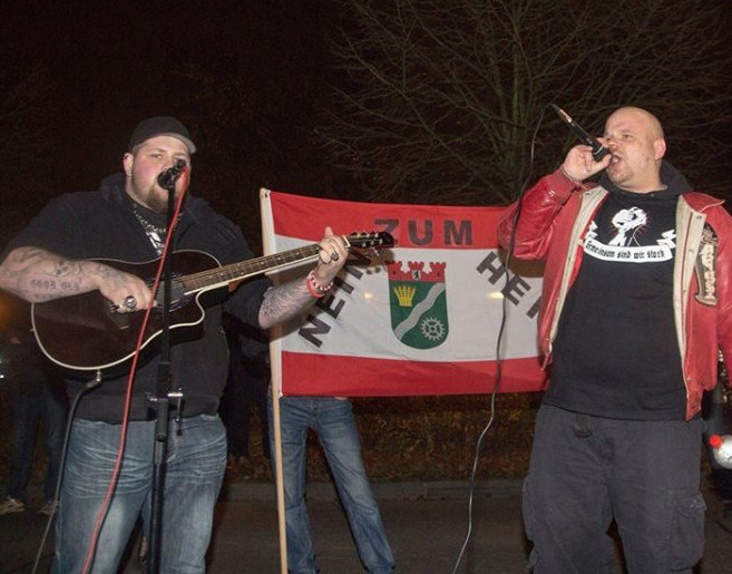 Das neonazistische Rap-Duo A3stus wird von den Musikern Villain051 und Mut zur Wahrheit (Berlin, Brandenburg) gebildet. Das Foto zeigt sie bei einem Auftritt im Rahmen eines Aufmarsches gegen die Einrichtung einer Unterkunft für Geflüchtete in Berlin 2015.