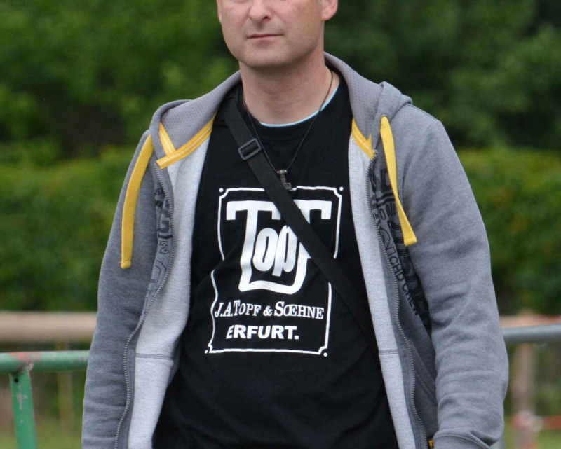 Das Logo der Firma »Topf und Söhne Erfurt«, das dieser Teilnehmer eines Neonazikonzertes 2017 zeigt, ist sein zynisches Bekenntnis zur Massenvernichtung im NS. Die Erfurter Firma Topf und Söhne hatte Verbrennungsöfen für Vernichtungslager und Türen von Gaskammern hergestellt und 1942 sogar das Patent für einen »Durchlaufofen für die Massenverbrennung von Leichen« erhalten.