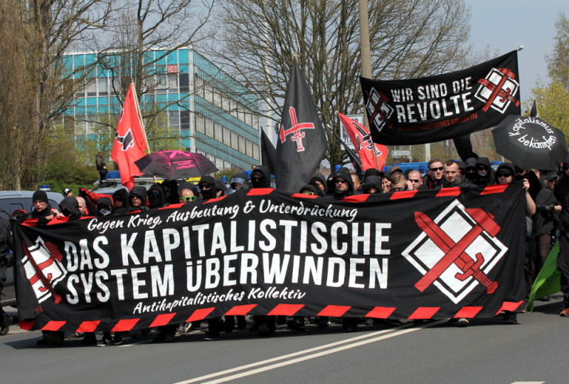Hammer und Schwert ist Teil des Gruppensymbols des Antikapitalistischen Kollektivs (AKK). Das AKK-Symbol ist auf den Transparenten rechts zu sehen.