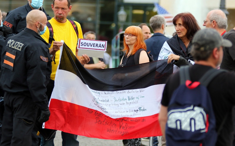 Die Reichsflagge mit aufgekritzelter Botschaft ist typisch für »Reichsbürger«. Das Bild zeigt Anhänger:innen der »Reichsbürger« bei einer Demonstration gegen die Maßnahmen zur Eindämmung der COVID-19-Pandemie im August 2020 in Berlin.