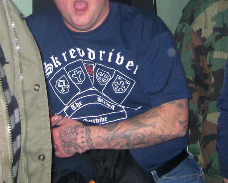 In der Mitte des Motivs ist das »S«-Logo der englischen Neonaziband Skrewdriver. Daneben sind u.a. die Abzeichen der 23. SS-Freiwilligen-Panzergrenadier-Division »Nederland« (links, mit Odal-Rune) und der 25. Waffen-Grenadier-Division der SS »Hunyadi« (rechts mit Pfeilkreuz).  Die Division »Nederland« bestand mehrheitlich aus niederländischen NS-Kollaborateuren, die Division »Hunyadi« wurde zum großen Teil von SS-Freiwilligen gebildet, die der faschistischen ungarischen Pfeilkreuz-Bewegung angehörten.