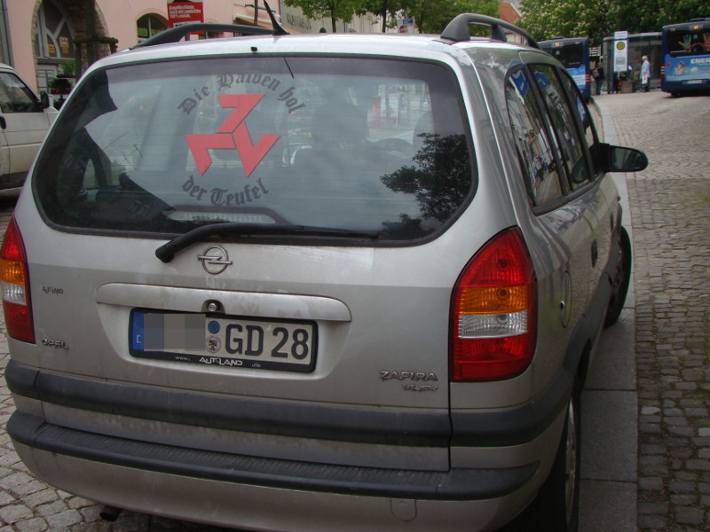 Neben der eckigen Triskele befindet sich auf der Heckscheibe des Autos der Spruch »Die Halben hol der Teufel«. Auch dies ist ein Bekenntnis zum Nationalsozialismus. Es ist ein Zitat der Film- und Romanfigur Gilbert Wolzow, der in dem antifaschistischen, in Ostdeutschland sehr bekannten Roman »Die Abenteuer des Werner Holt« ein jugendlicher Flakhelfer und begeisterter Nazi ist. Obgleich er den Untergang vor Augen hat spornt er seine Kameraden mit flammenden Reden zum Durchhalten an. Einer seiner Sprüche ist: »Wer . . . Deutschland in seiner schwersten Stunde im Stich lässt, der ist ein Schweinehund. Alles oder nichts. Die Halben hol' der Teufel. Wir stehen zum Führer.«