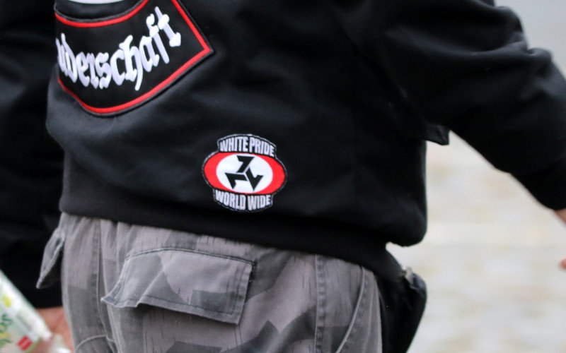 Die eckige Triskele in der Gestaltung als Hakenkreuzfahne ist das Symbol der militant rassistischen Afrikaner Weerstandsbeweging (AWB). Die AWB ist eine weltweit bekannte Organisation neonazistischer weißer Buren in Südafrika. Der Aufnäher auf diesem Bild wurde 2019 von einem Neonazi in Sachsen gezeigt.