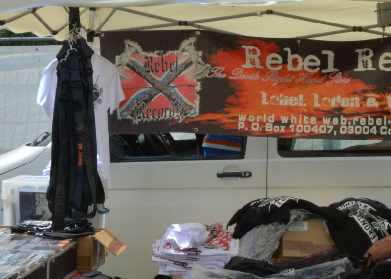 Unverkennbare Elemente der Südstaatenfahne im Logo des Cottbusser Neonazi-Labels Rebel Records, gezeigt auf einem Werbetransparent auf einem Neonazi-Konzert in Thüringen 2017.