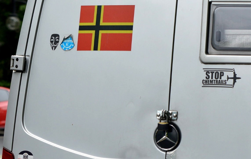 Das Heck des Autos zeigt die Aufkleber »STOP CHEMTRAILS« und »EU DIKTATUR NEIN DANKE!«. Desweiteren sind als Symbole die stilisierte Anonymous-Maske und die Wirmer-Flagge zu sehen.