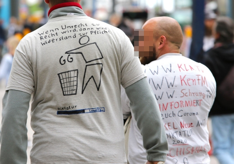 Sogenannte »Hygiene-Demos« richten sich gegen die Maßnahmen und Verordnungen, die aufgrund der COVID-19-Pandemie erlassen werden. Die Teilnehmenden inszenieren sich als Rebell*innen gegen eine Diktatur. Für Aufklärung und Wahrheit würden sogenannte »Alternative Medien« sorgen. Dieses Label knüpft an den Begriff »Alternativen Fakten« an, der 2017 von der Jury der Sprachkritischen Aktion zum Unwort des Jahres 2017 bestimmt wurde. Laut der Jury sei die Bezeichnung »der verschleiernde und irreführende Ausdruck für den Versuch, Falschbehauptungen als legitimes Mittel der öffentlichen Auseinandersetzung salonfähig zu machen«. Zu den Medien, die die abgebildete Person auf ihrem Shirt bewirbt, zählen die Video-Kanäle von Ken Jebsen (KenFM) und Heiko Schrang (Schrang TV).